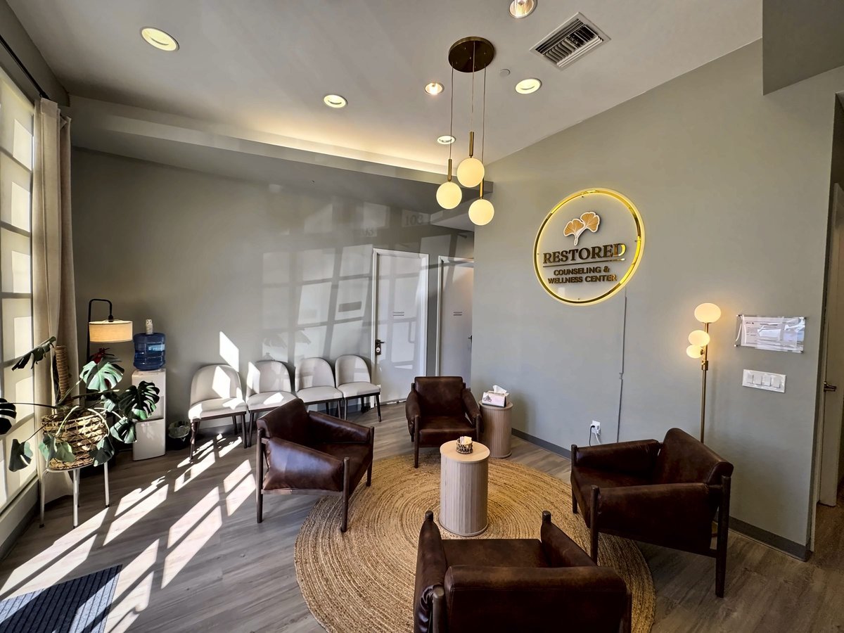 Modern office waiting room with brown leather chairs, round wooden table, pendant lights, and large windows with natural sunlight